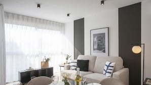 A modern living room with a sofa, dining table, and a large window with sheer curtains.