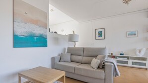Ett vardagsrum med en soffa, ett träbord, en lampa och en tavla som föreställer en våg.