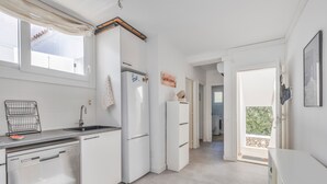 Ett modernt kök med vita skåp, diskmaskin, kylskåp och ett fönster med gardin.