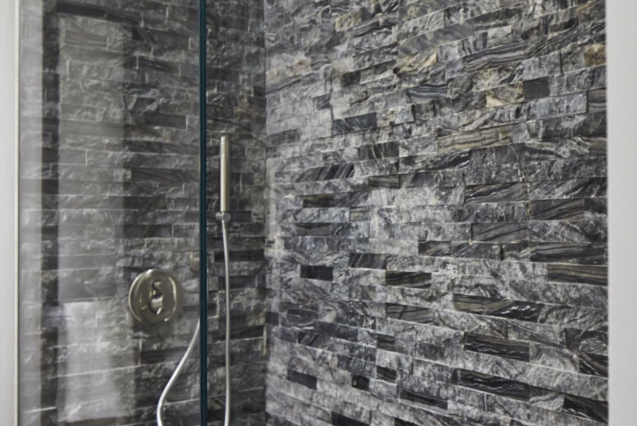 Eine Dusche mit Glastür und Wand mit Steinoptik.