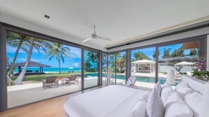 Een slaapkamer met een groot bed, een plafondventilator en uitzicht op een zwembad en palmbomen.