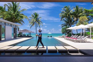 A poolside area with lounge chairs and umbrellas, palm trees, and a clear view of the ocean. - Villa Malee Sai (Takua Thung)