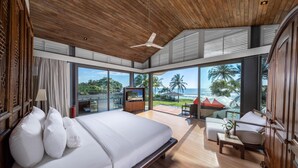 Een ruime slaapkamer met een groot bed, een plafondventilator en uitzicht op de oceaan door grote ramen.