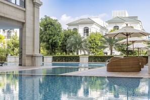 A swimming pool with lounge chairs and umbrellas, surrounded by greenery and a large building with a tiled roof. - Meliá Vinpearl Hai Phong Rivera (Hai Phong)