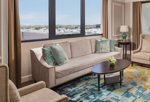 A hotel room with a sofa, armchair, coffee table, and a view of the cityscape through large windows. - MeliĆ” Vinpearl Hai Phong Rivera (Hai Phong)