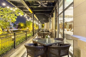 Een terras buiten met rieten meubels, een glazen tafel en een decoratieve vaas.
