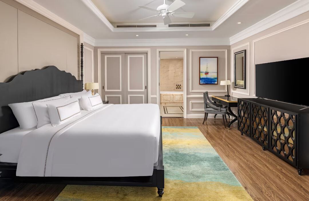 A hotel room with a bed, a desk, a TV, and a seating area.