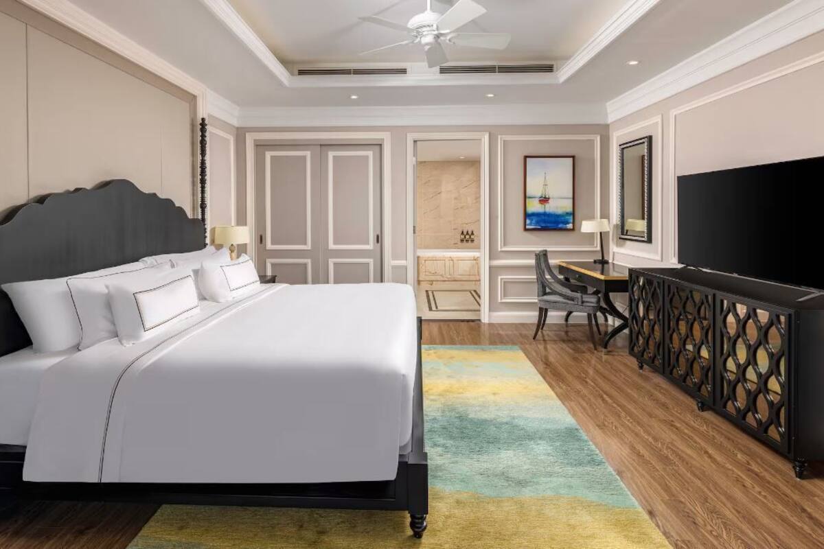 Quarto de hotel com uma cama grande, uma escrivaninha, uma televisão e um espaço de estar.