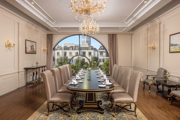 A formal meeting room with a long table, chairs, a chandelier, and a view through a large arched window. - MeliĆ” Vinpearl Hai Phong Rivera (Hai Phong Municipality)