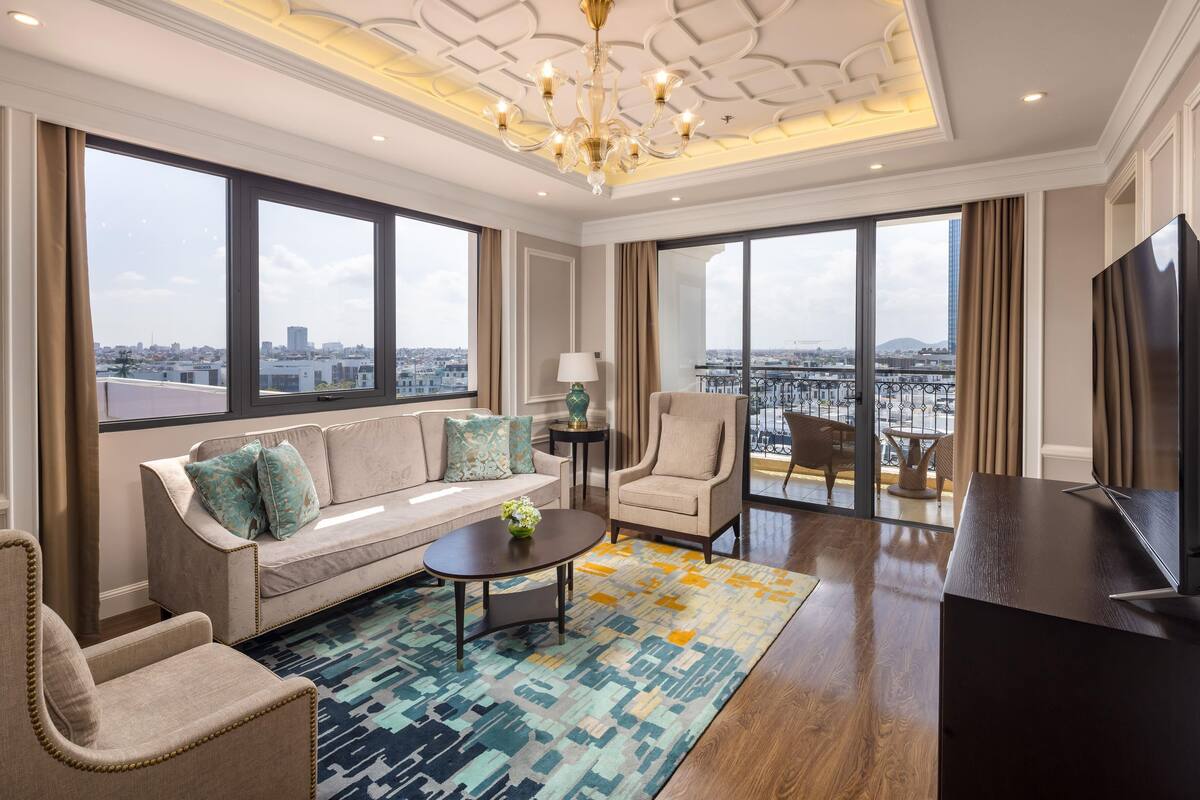 Quarto de hotel moderno com sofá, poltrona, mesa de centro e televisão.