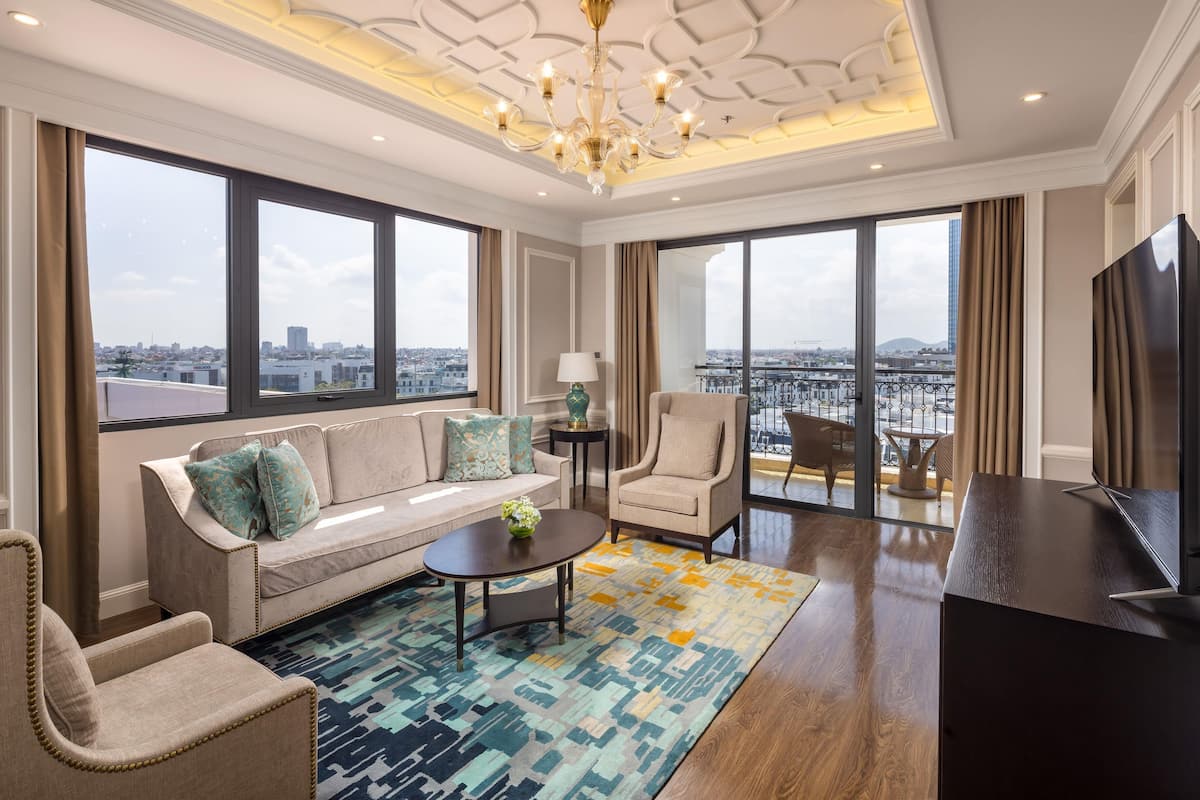 A modern hotel room with a sofa, armchair, coffee table, and a TV.
