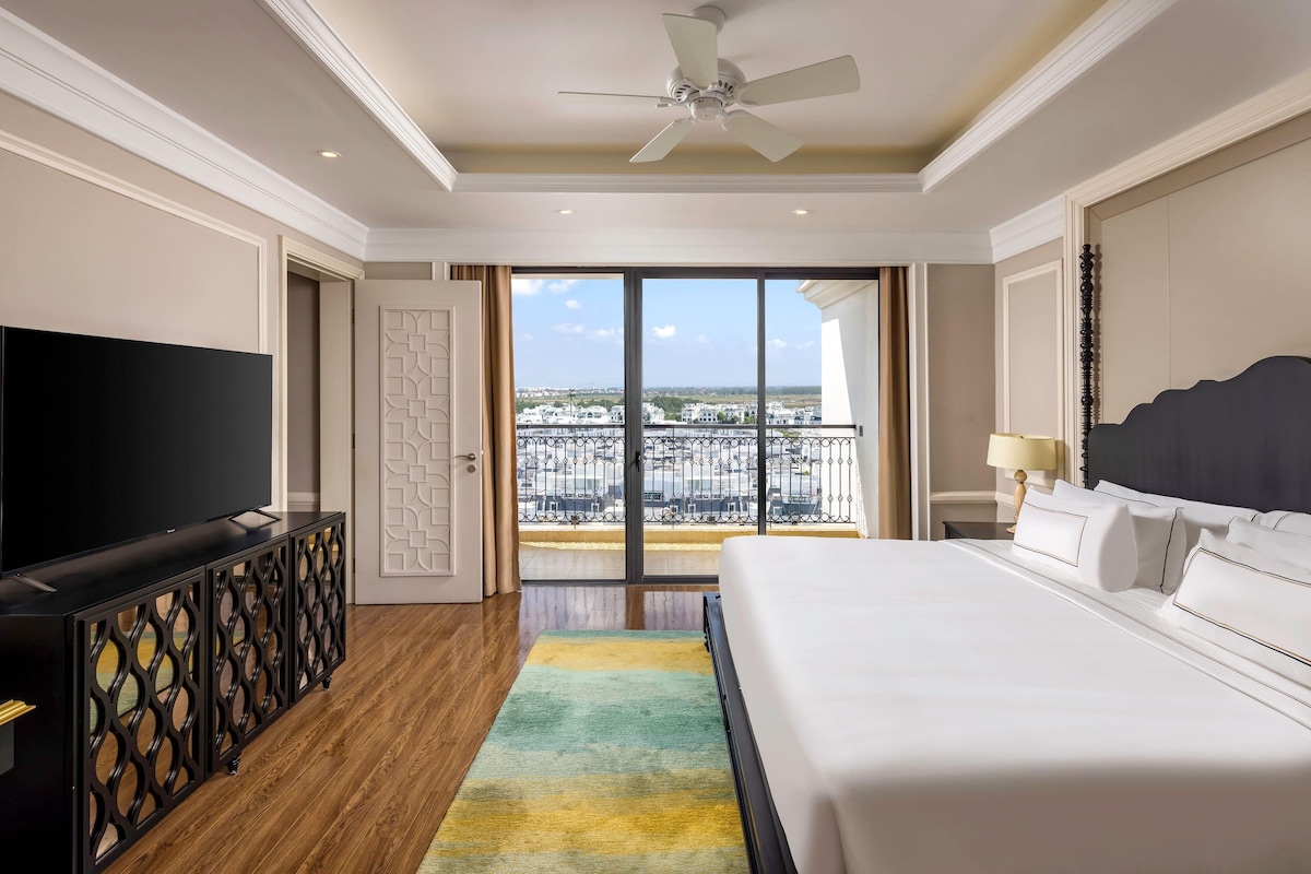 Quarto de hotel com cama, televisão, varanda e ventoinha no teto.