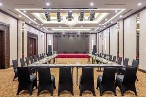A conference room with a long table, chairs, a stage, and a chandelier. - MeliĆ” Vinpearl Hai Phong Rivera (Hai Phong)