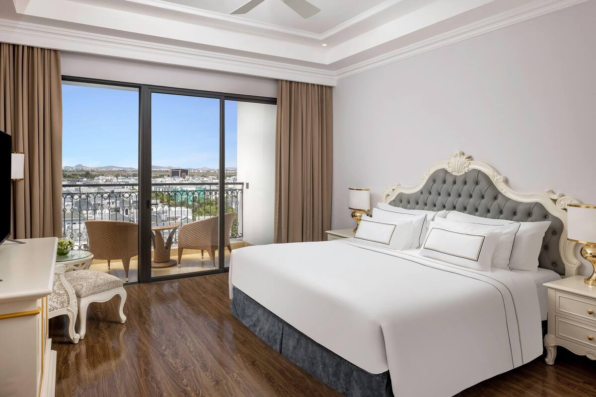 Quarto de hotel com uma cama grande, uma escrivaninha, uma cadeira e varanda com vista para a cidade.
