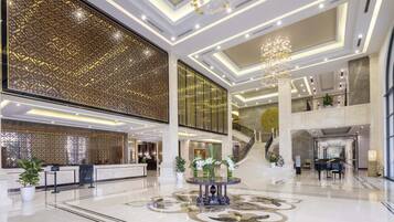 A spacious lobby with a grand piano, a reception desk, and a decorative wall.