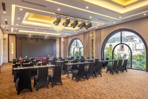 A conference room with tables, chairs, a stage, and large windows with a view of buildings. - MeliĆ” Vinpearl Hai Phong Rivera (Hai Phong Municipality)