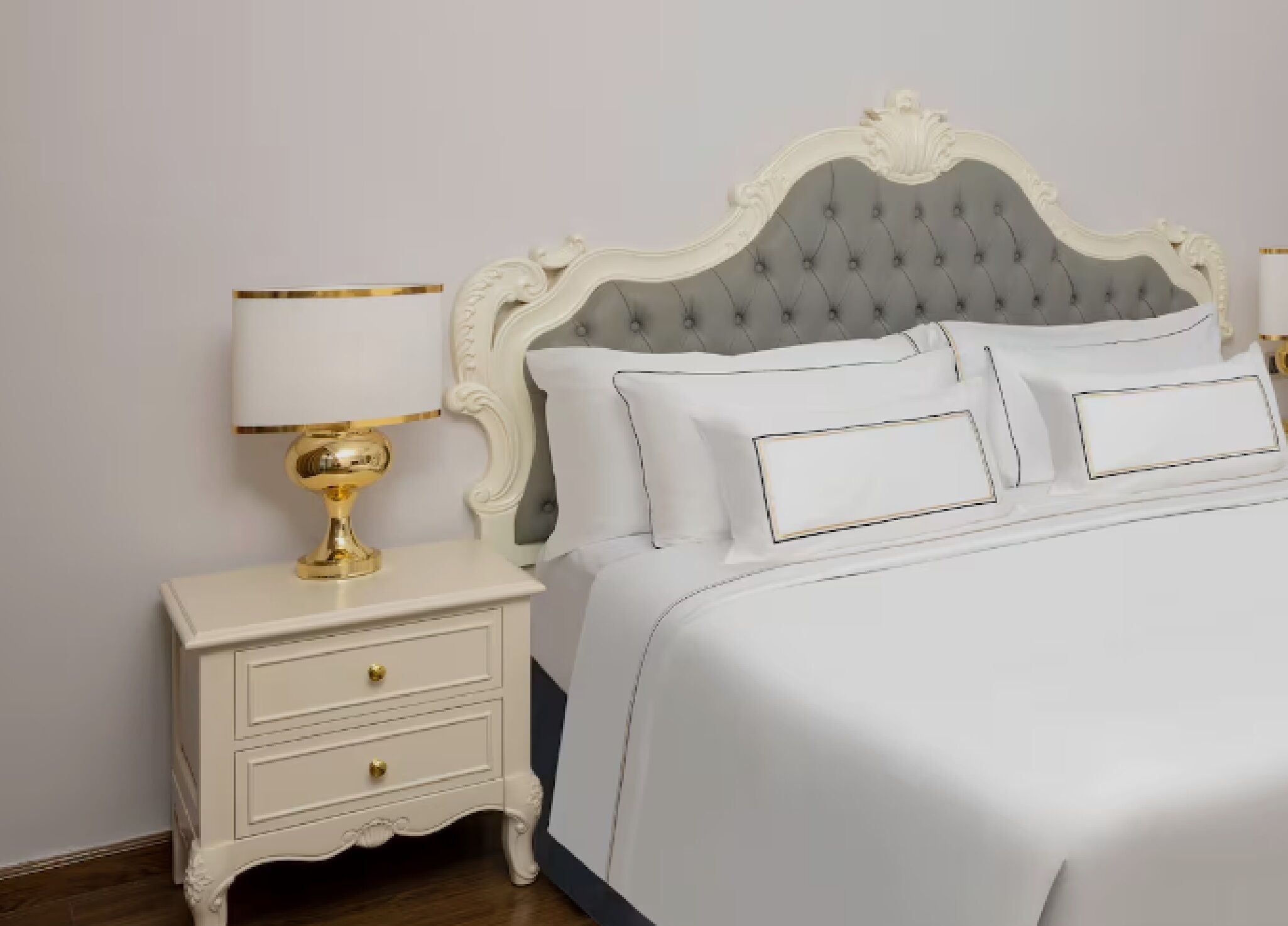 A bed with a tufted headboard, white bedding, and a gold lamp on a nightstand.