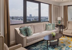Moderni hotellihuone, jossa on suuri ikkuna, sohva, sohvapöytä ja tuoli.