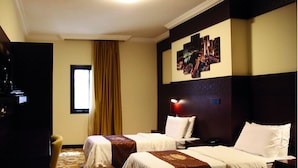 A hotel room with two beds, a large window with curtains, a cityscape artwork on the wall, and a carpeted floor. - AlFajr AlBadie Hotel 1 (Makkah)