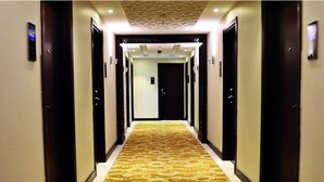 A hotel hallway with a patterned carpet, doors on both sides, and a ceiling with recessed lighting. - AlFajr AlBadie Hotel 1 (Makkah)