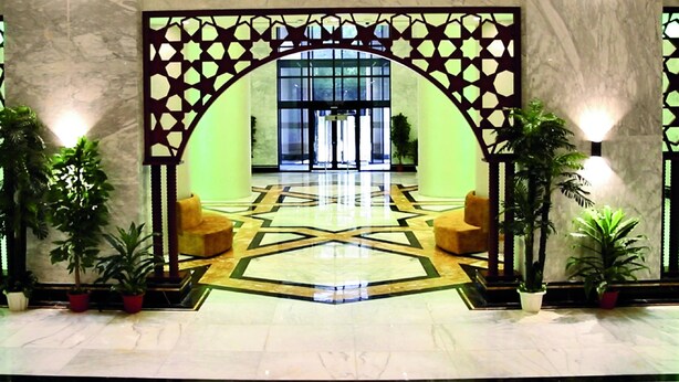 A lobby with a geometric floor pattern, a large arched entrance, and potted plants. - AlFajr AlBadie Hotel 1 (Makkah)