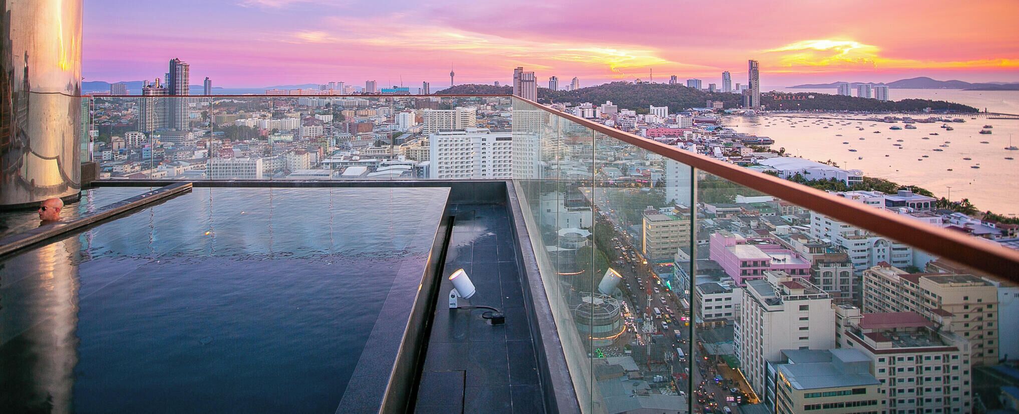 A rooftop pool with a city view, glass railings, and a sunset.