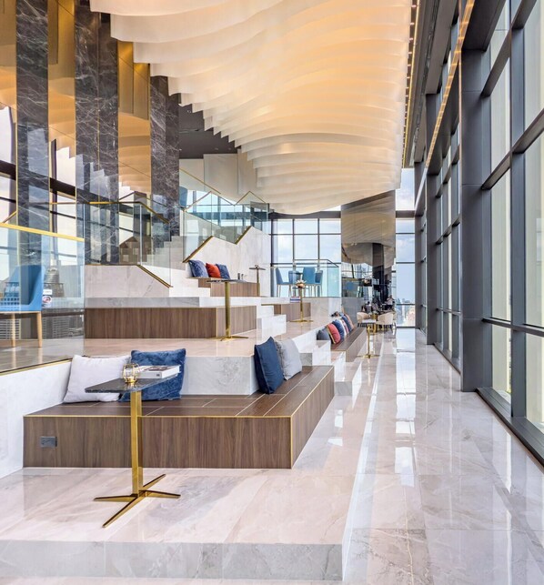 Un vestíbulo amplio con diseño moderno, que cuenta con una zona de estar central, una escalera y ventanas grandes.