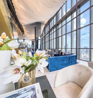 A modern hotel lobby with a high ceiling, large windows, and a view of the cityscape. - Luxury Downtown Bangkok 2BR 2BA · Sky Pool Gym · 5min Walk to Siam Paragon (Bangkok)