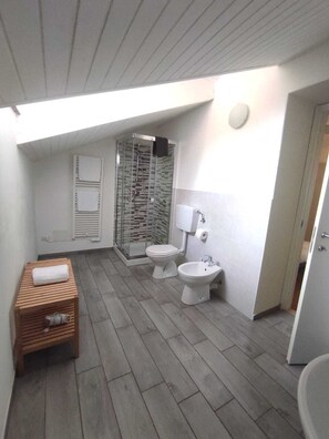 A small, modern bathroom with a shower, toilet, bidet, and a wooden bench.