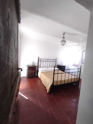 A bedroom with a metal bed frame, a wooden nightstand, a dresser, and a chandelier.