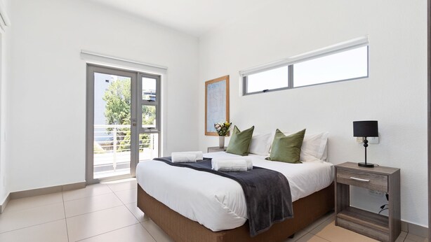 A modern bedroom with a large bed, a nightstand, a window, and a view of the outdoors. - Insignia 312 (Johannesburg)