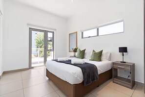 A modern bedroom with a large bed, a nightstand, a window, and a view of the outdoors. - Insignia 312 (Johannesburg)