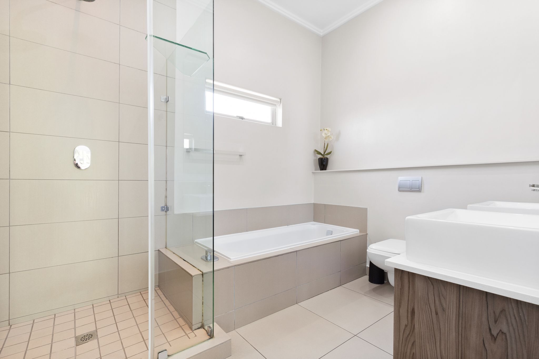 A modern bathroom with a glass-enclosed shower, a large bathtub, and a wooden vanity.