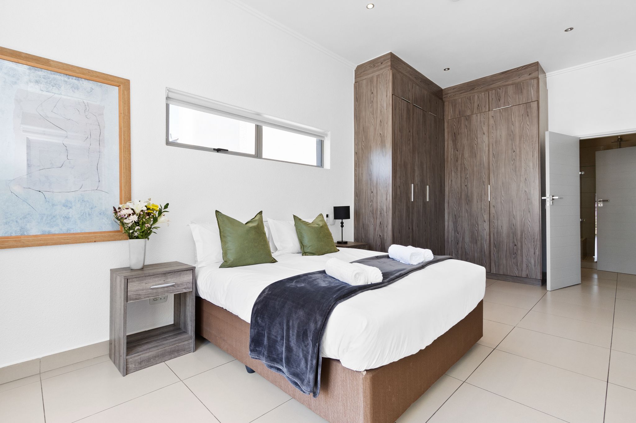 Ein modernes Schlafzimmer mit einem großen Bett, einem Holzschrank und einem Nachttisch mit Blumen.