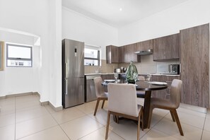 A modern kitchen with a dining area, featuring a stainless steel refrigerator, wooden cabinets, and a round dining table with chairs. - Insignia 312 (Johannesburg)