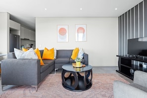 Ein modernes Wohnzimmer mit einem grauen Ecksofa, einem runden Couchtisch und einem Flachbildfernseher.