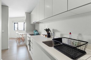 A modern kitchen with white cabinets, a sink, and a countertop. There is a window with a view of trees outside. - 806 2six2 Florida Road (Durban)