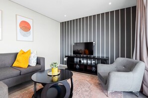 A modern living room with a sofa, armchair, coffee table, and a TV on a black stand. - 806 2six2 Florida Road (Durban)