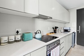 A modern kitchen with white cabinetry, a black induction cooktop, a teal kettle, and labeled jars for sugar, coffee, and tea.
