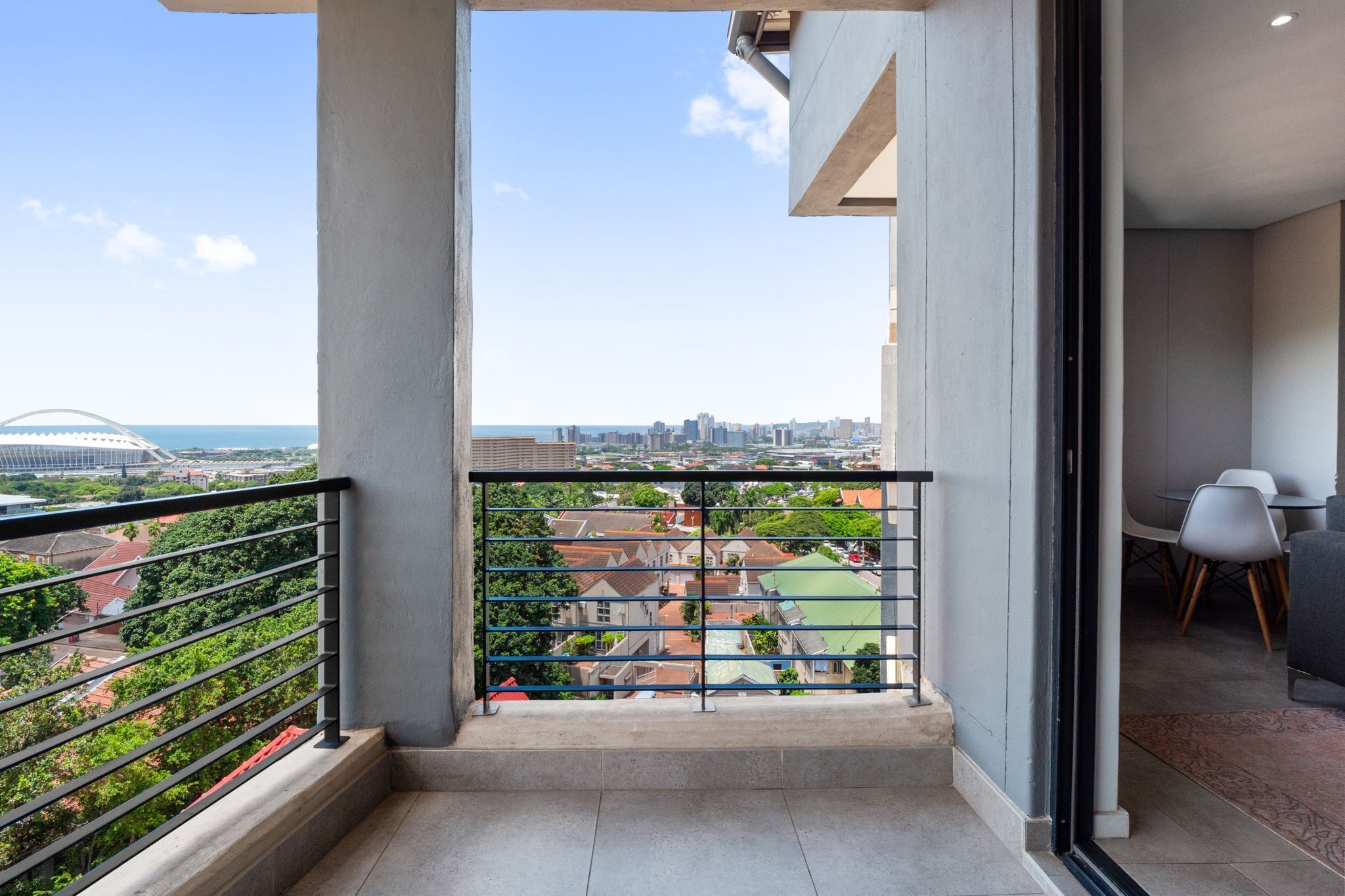Un balcón con vistas a la ciudad, una zona de comedor con sillas modernas y suelo de hormigón.