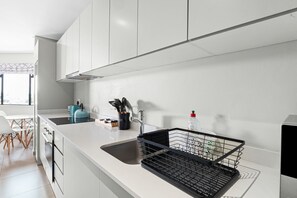 A modern kitchen with white cabinets, a black dish rack, and a blue kettle.
