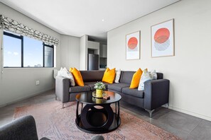 A modern living room with a grey sofa, orange cushions, a black coffee table, and a patterned rug.