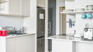 Una cocina moderna con armarios blancos, un refrigerador de acero inoxidable y una cafetera.
