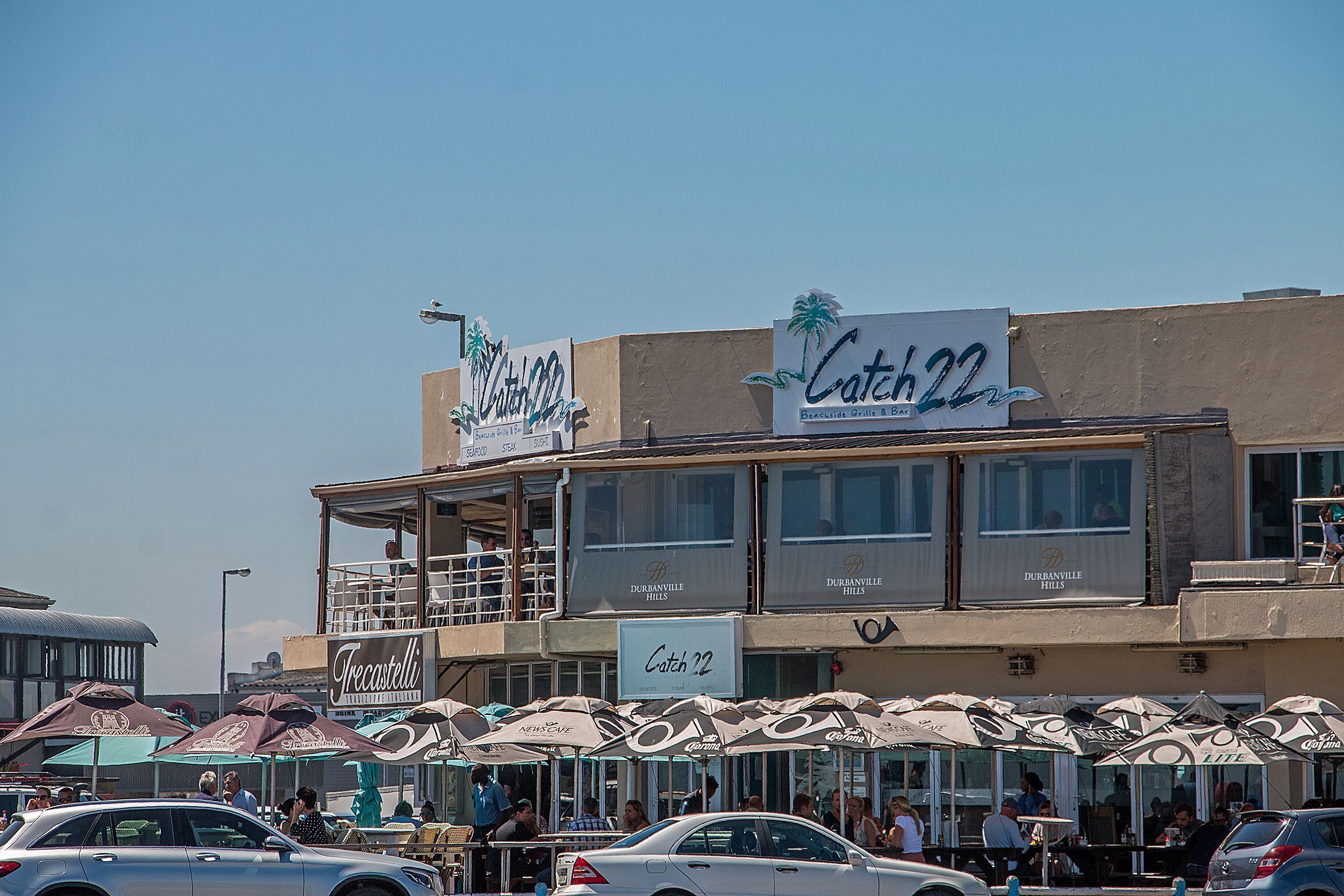 A building with outdoor seating and umbrellas, labeled "Catch 22" and "Trecastelli."