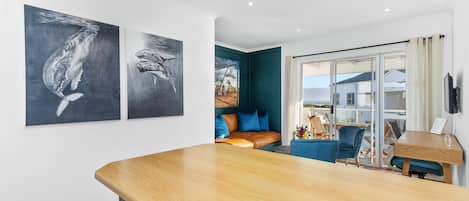 A modern kitchen with a wooden countertop, a seating area with a blue sofa and a dining table, and artwork on the walls.