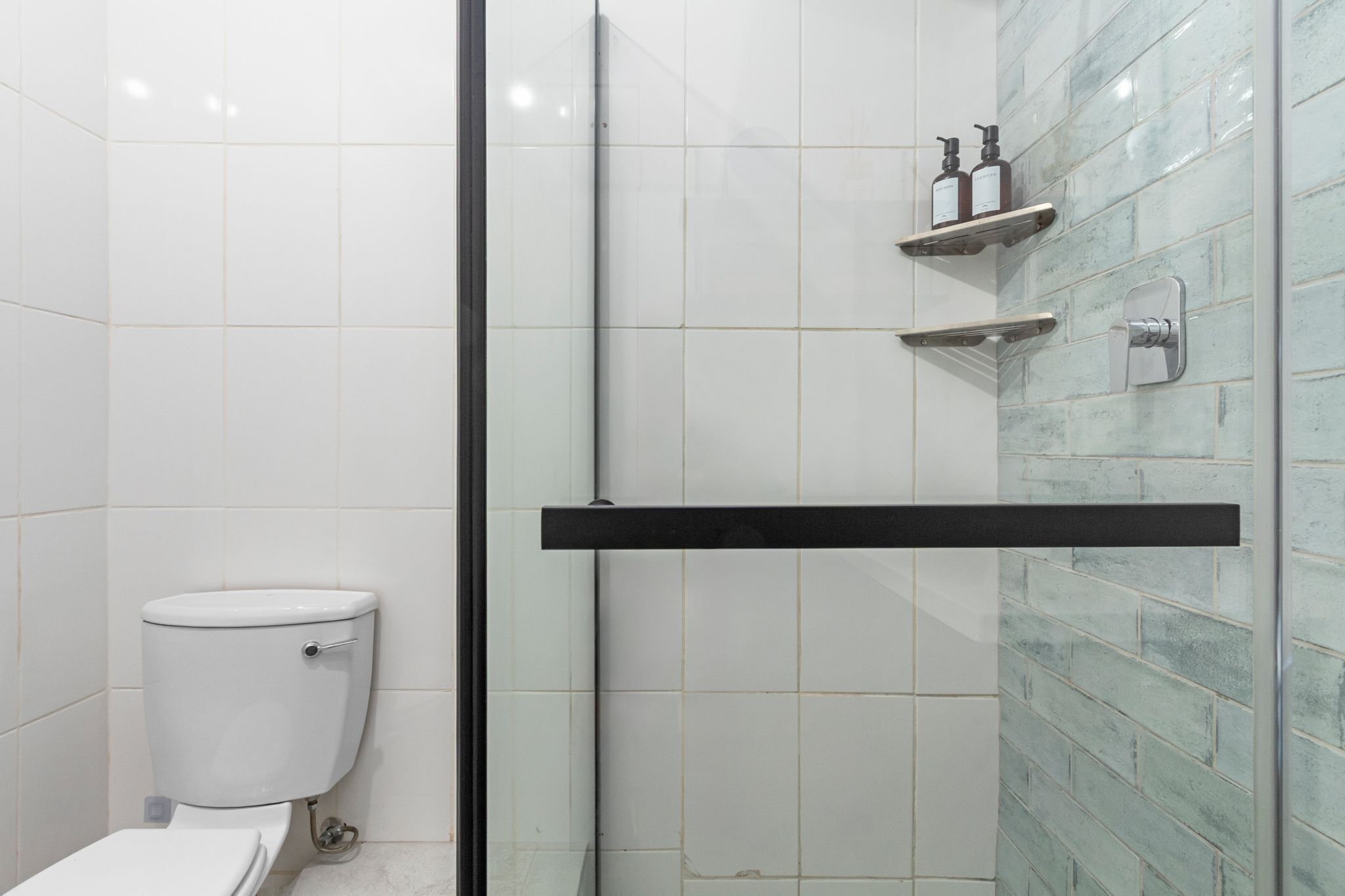 A modern bathroom with a glass-enclosed shower, white tiles, and a toilet.