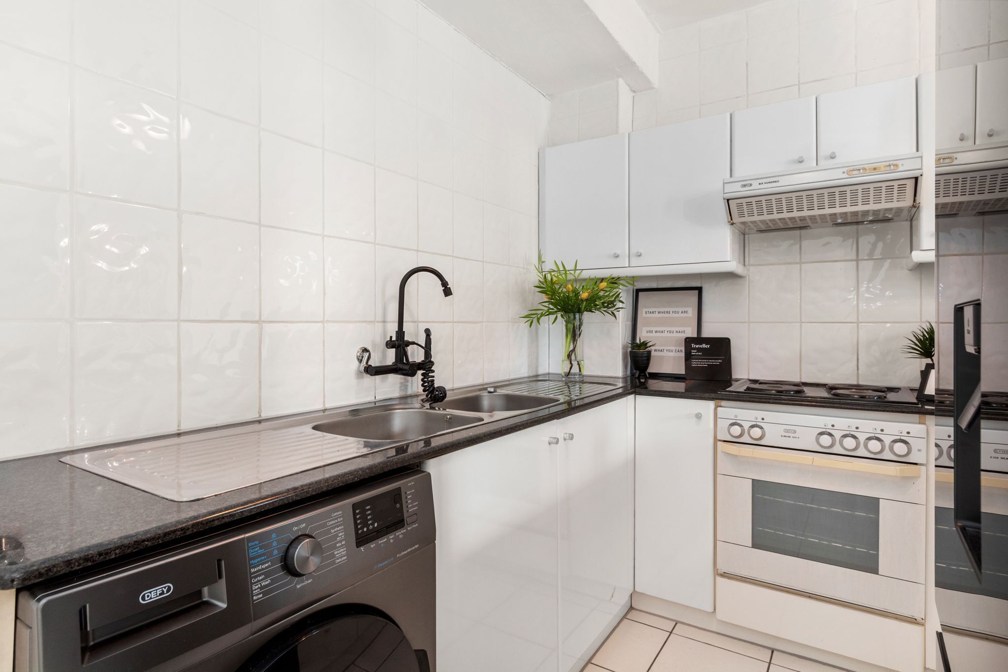 A modern kitchen with white cabinets, a black countertop, a built-in dishwasher, a stove, and a sink.