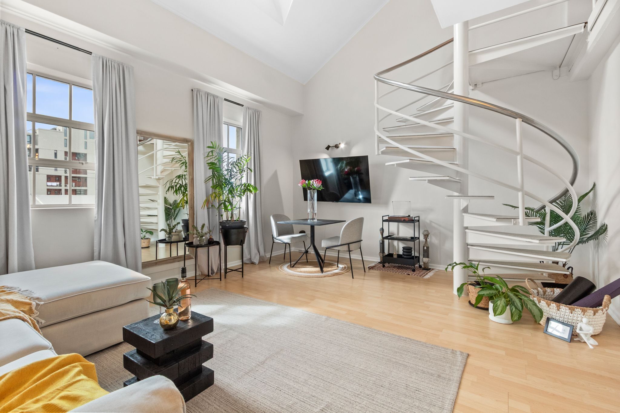 A modern living room with a spiral staircase, a flat-screen TV, and a dining area with a round table.