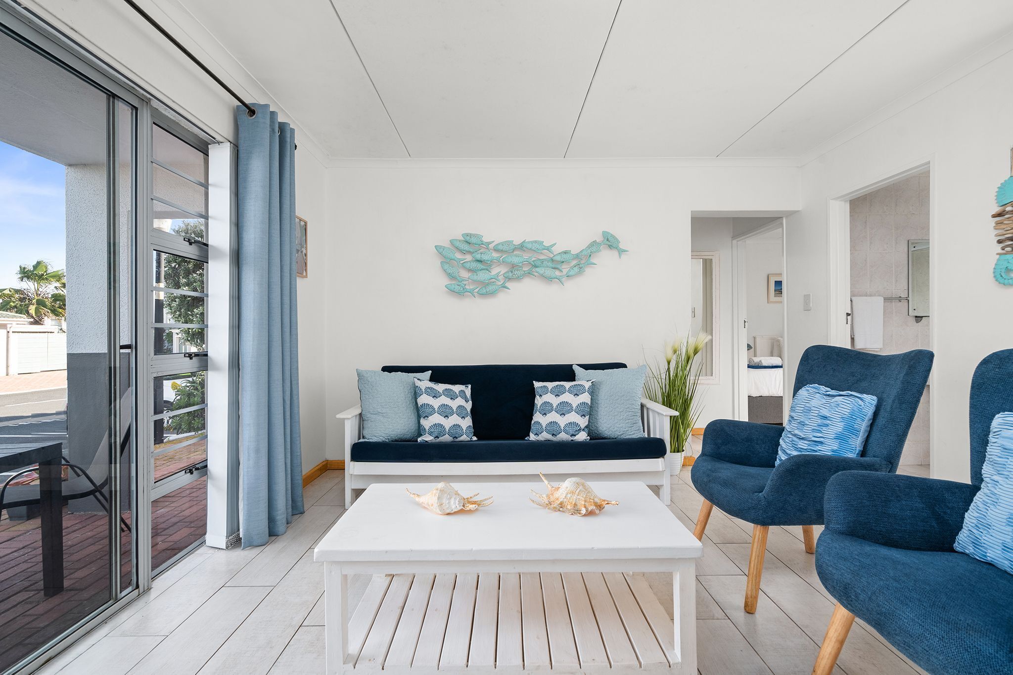 A modern living room with a white sofa, blue armchairs, a white coffee table, and decorative shells.