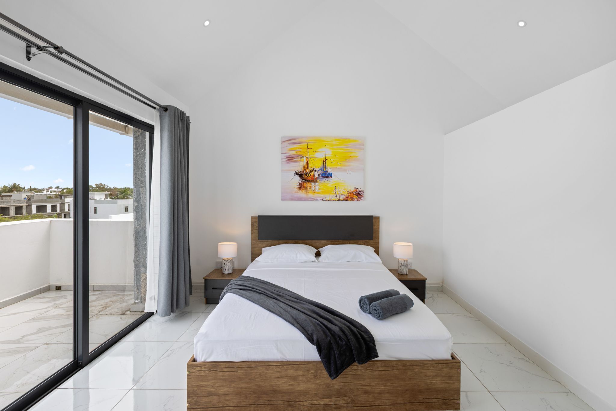 Ett modernt hotellrum med en stor säng, en tavla ovanför sängen och utsikt över staden från balkongen.